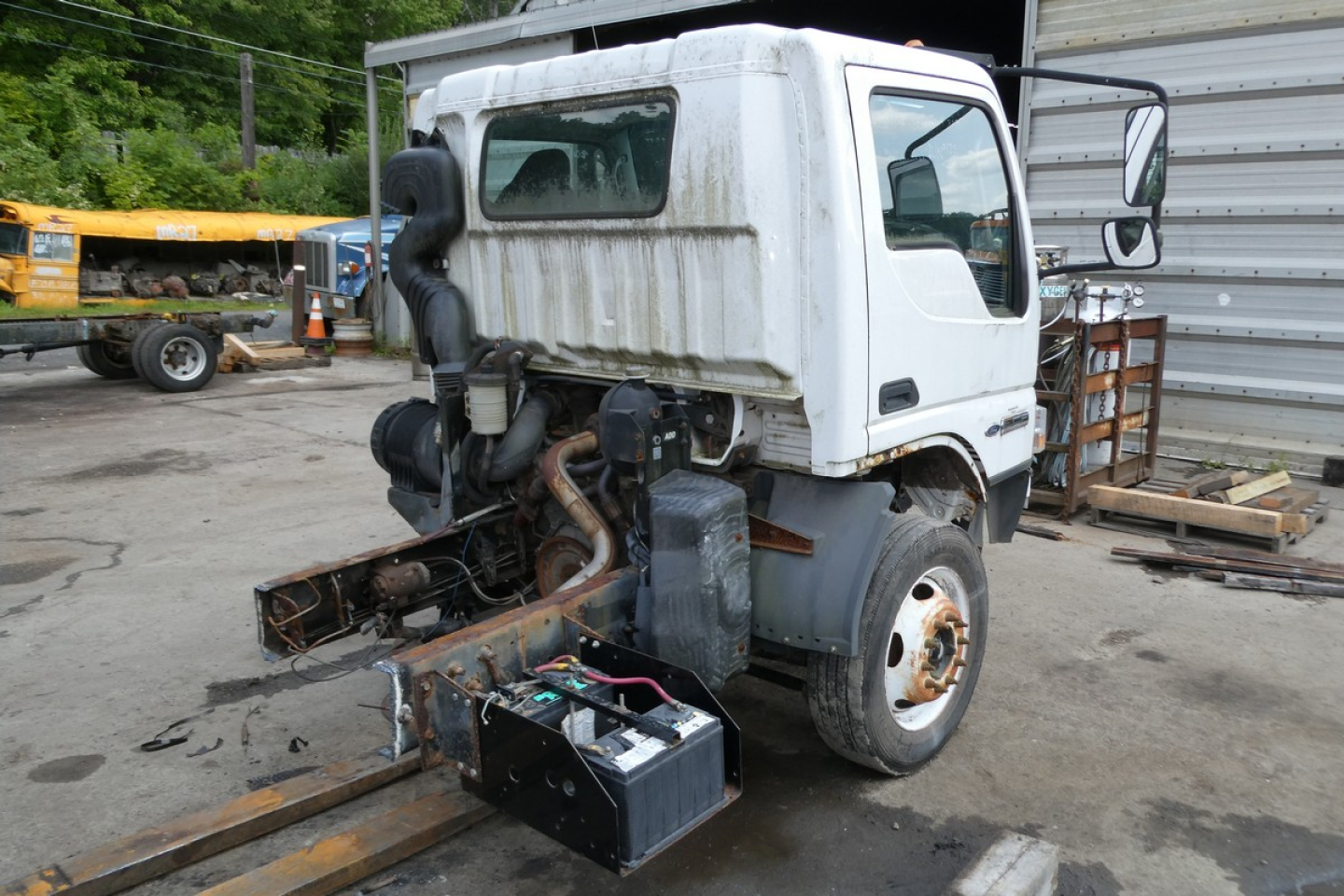 Ford LCF cab and chassis truck with exposed engine and battery tray in a yard.