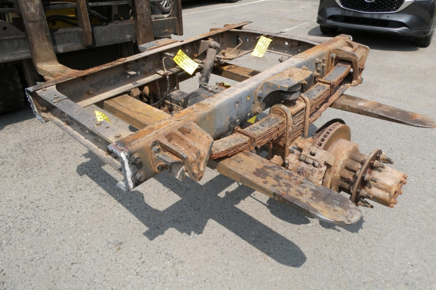 Chassis frame and rear axle assembly with rusted metal, mounting brackets, and hydraulic lines/hoses visible.