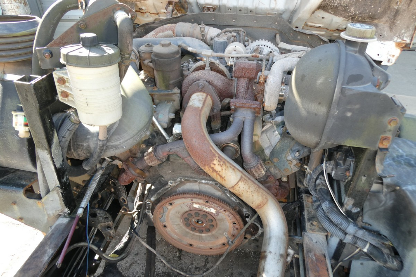 View of Ford LCF engine bay showing turbo manifold and exhaust pipe, coolant reservoir, belts, and various hoses.