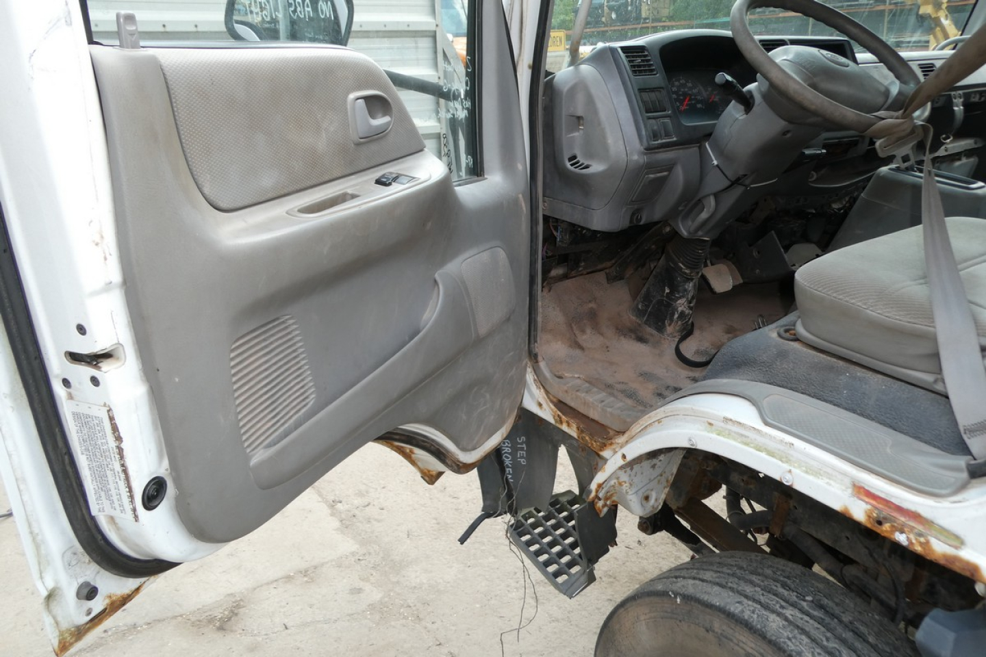 Ford LCF cab and chassis interior with manual door panel and exposed steps; steering wheel and driver area visible from open door, showing worn floor area and dashboard.