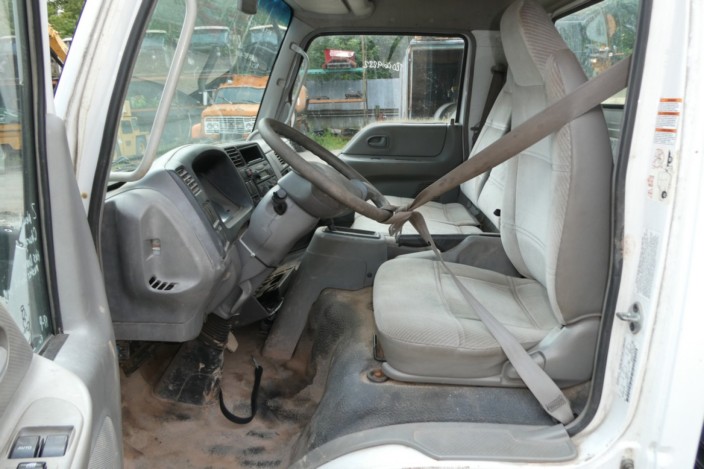 Cab and chassis truck interior showing steering wheel and driver seat with seatbelt, dusty floor, and gray dashboard.