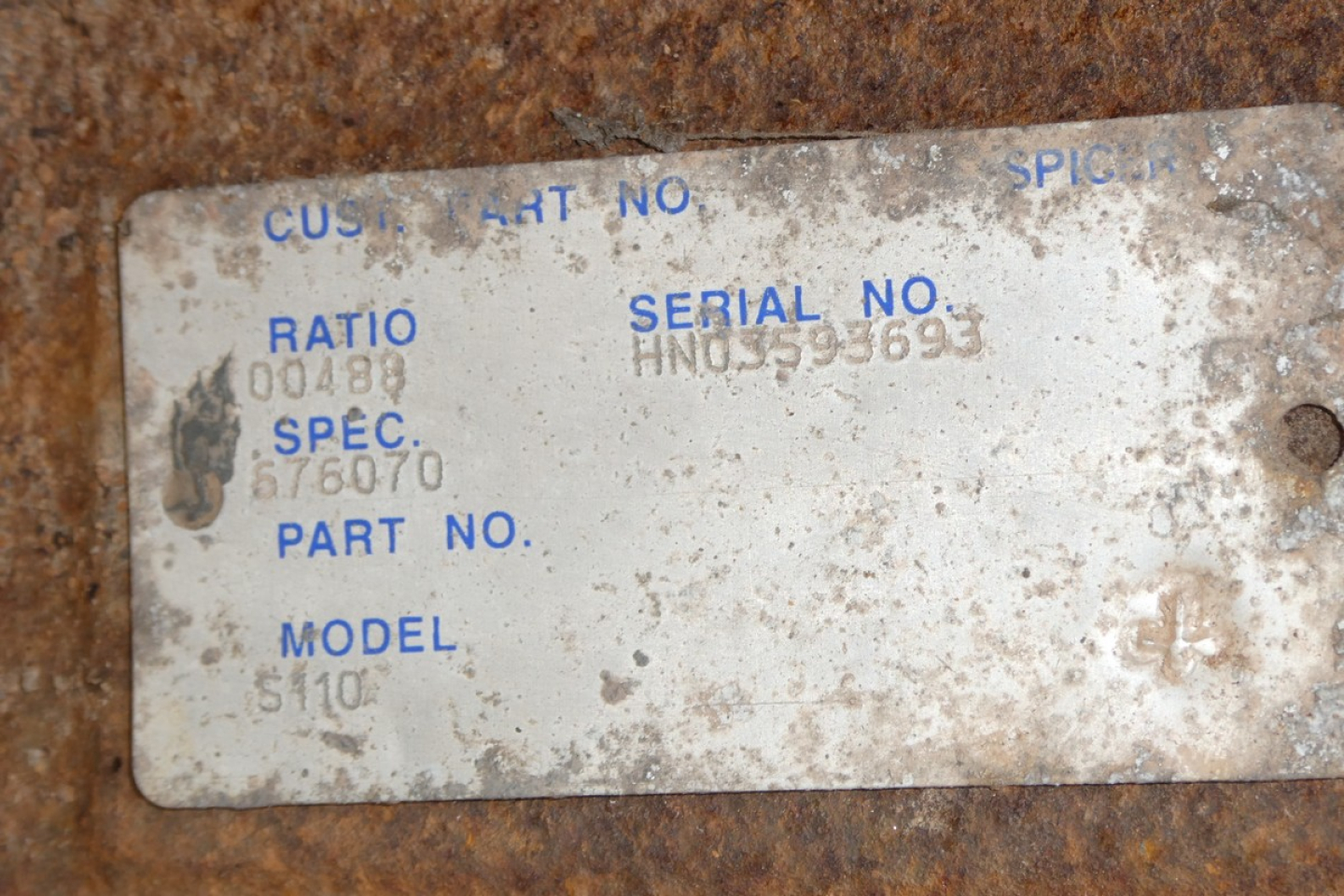 Tag showing serial number and model information on a rusted surface; text includes SERIAL NO., SPEC., PART NO., MODEL 5110, and various numeric fields.