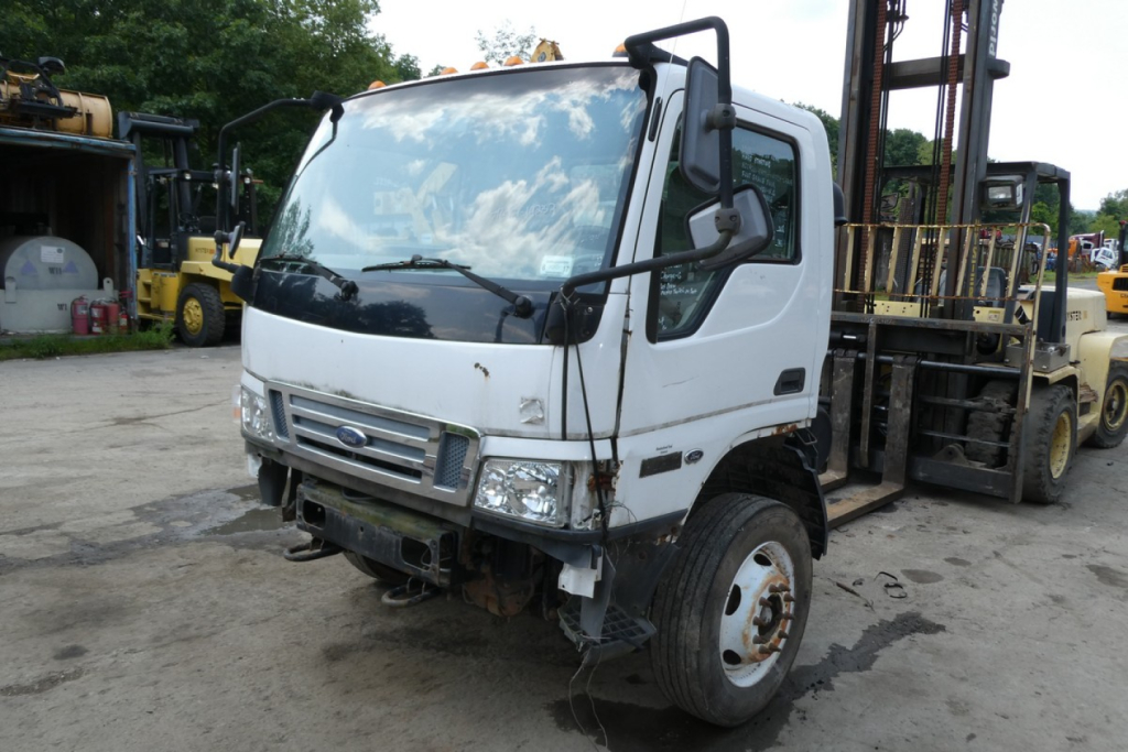 Ford LCF cab and chassis truck showing front and passenger side, white cab, visible forklift in background, stock and VIN notations not visible.