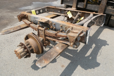 Wheel hub and axle assembly showing rusty undercarriage and suspension components with mounting brackets and tag labels.