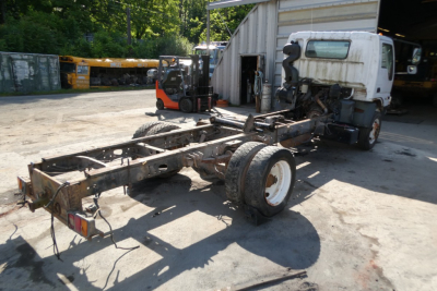 Ford LCF cab and chassis frame with cab removed, single rear axle, white cab, in a yard.