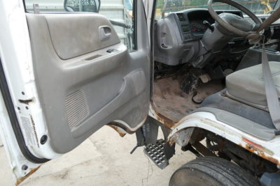 Ford LCF cab and chassis interior with manual door panel and exposed steps; steering wheel and driver area visible from open door, showing worn floor area and dashboard.