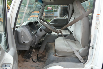 Cab and chassis truck interior showing steering wheel and driver seat with seatbelt, dusty floor, and gray dashboard.