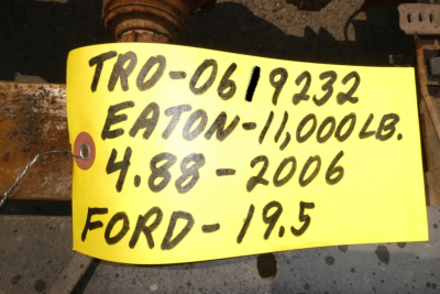 Handwritten yellow tag with black text reading: 'TRO-0619232 EATON-11,000LB. 4.88 - 2006 FORD- 19.5' attached to a metal surface.