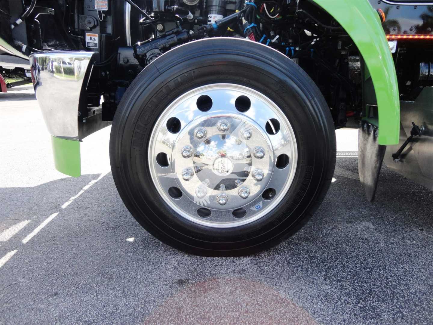 Peterbilt truck front wheel and chrome hubcap with green fender in view; some mechanical components visible behind the wheel.