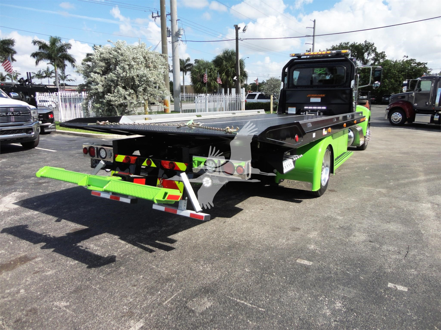Truck bed of green rollback tow truck showing flatbed with rear ramps and reflective safety tape.