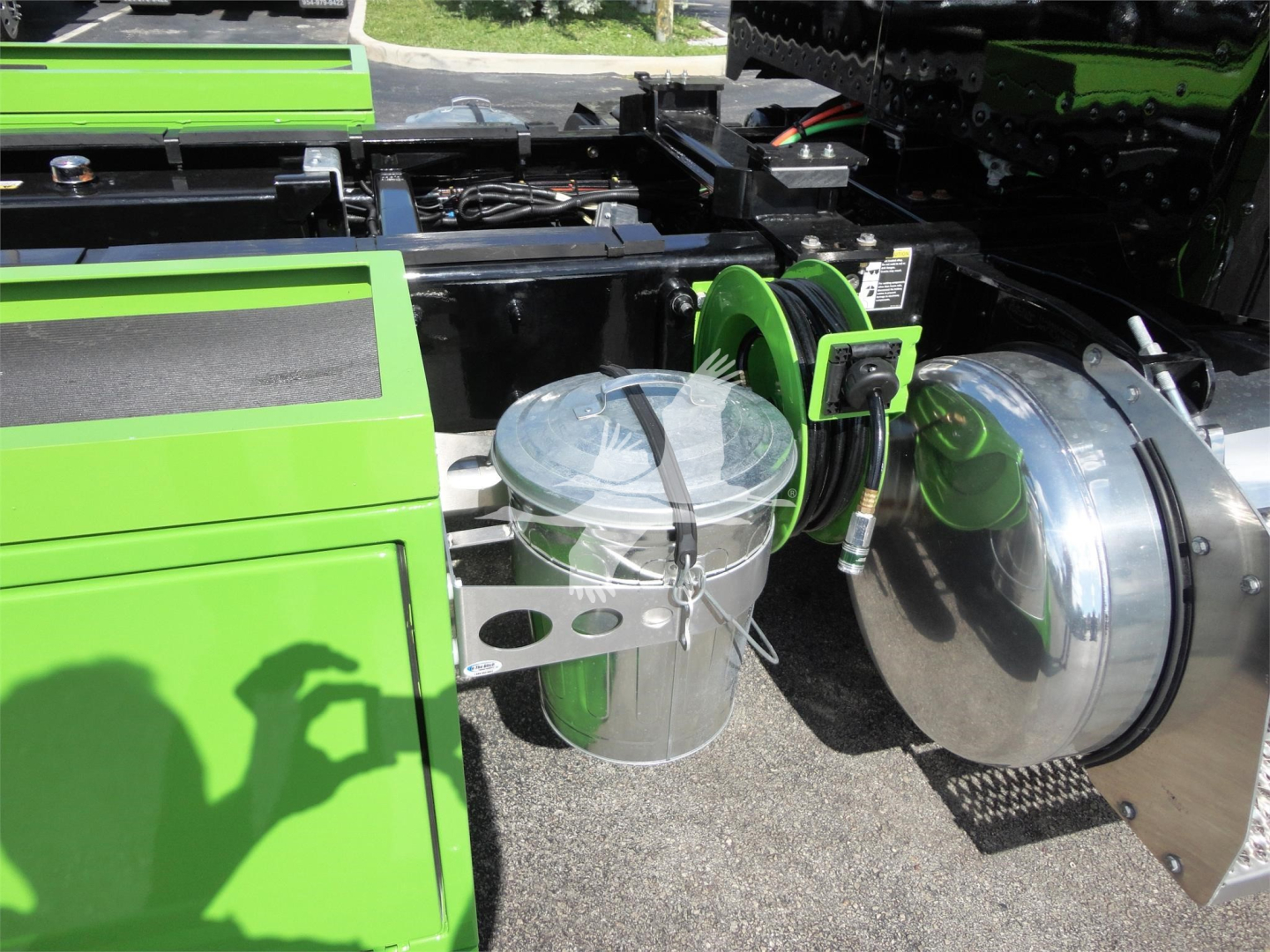 Truck equipment bay showing a bright green Peterbilt 337 rollback chassis with chrome air tanks and green hose reel assembly.