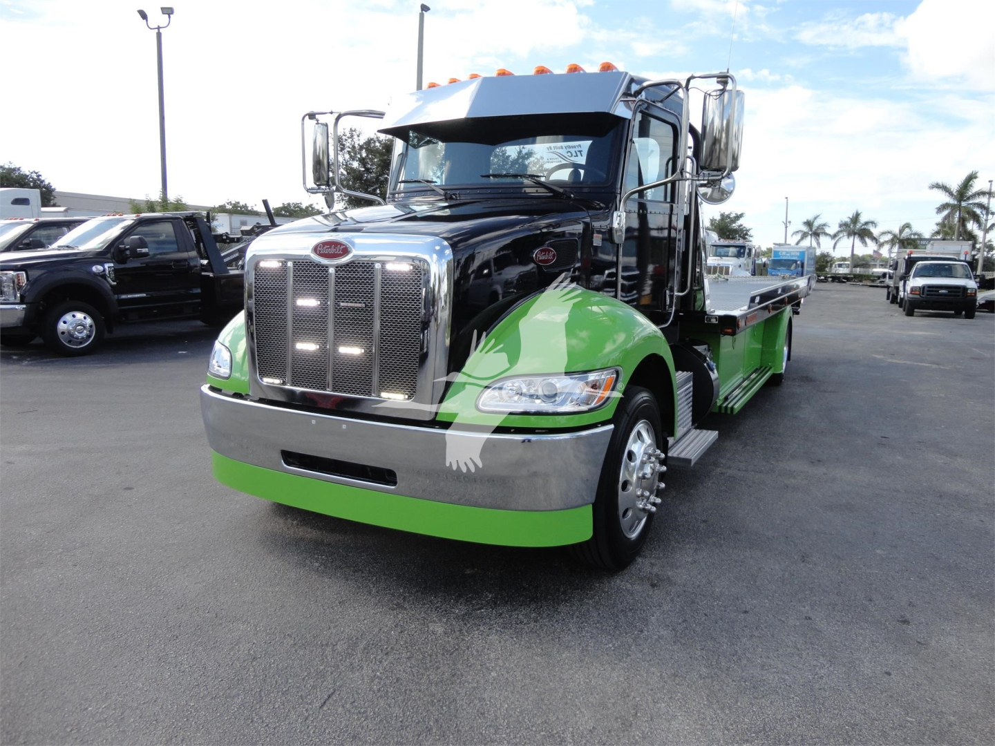 Peterbilt 337 rollback truck front view with black cab and bright green side accents and chrome grille; dealership lot in background.