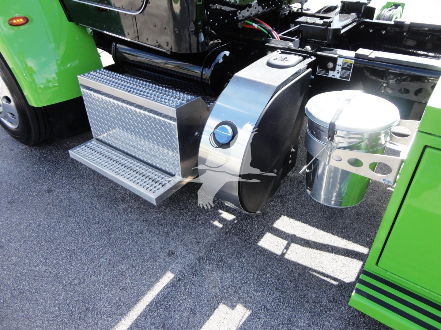 Step/footboard and cylindrical air reservoir on green Peterbilt truck, with chrome cylindrical fuel filter or air tank and diamond-plate step near chassis.