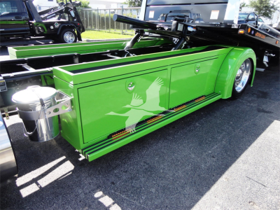 Green Peterbilt rollback bed side panel with crane mechanism and white bird graphic, chrome accents, side steps, and black truck bed in background.