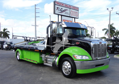 Peterbilt 337 rollback truck in green and black color scheme, side view showing chrome grille, front bumper, and flatbed; TLC Truck Sales Center sign in background.