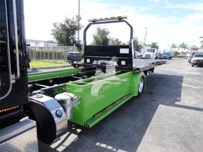 Peterbilt 337 rollback truck chassis with green tool/storage body and flatbed, side view showing hydraulic components and warning lights.