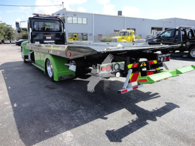 Peterbilt 337 rollback truck in green with hydraulic flatbed in raised position, rear view showing tail lights and deck, stock number J56607.