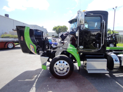 Truck cab side view with engine hood open showing green and black Peterbilt cab, chrome wheel, aluminum steps, and front fender area.