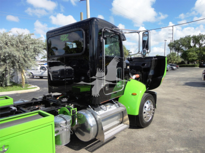Peterbilt 337 truck side view with black cab and green fenders, chrome fuel tanks, and open door; rollback equipment visible.