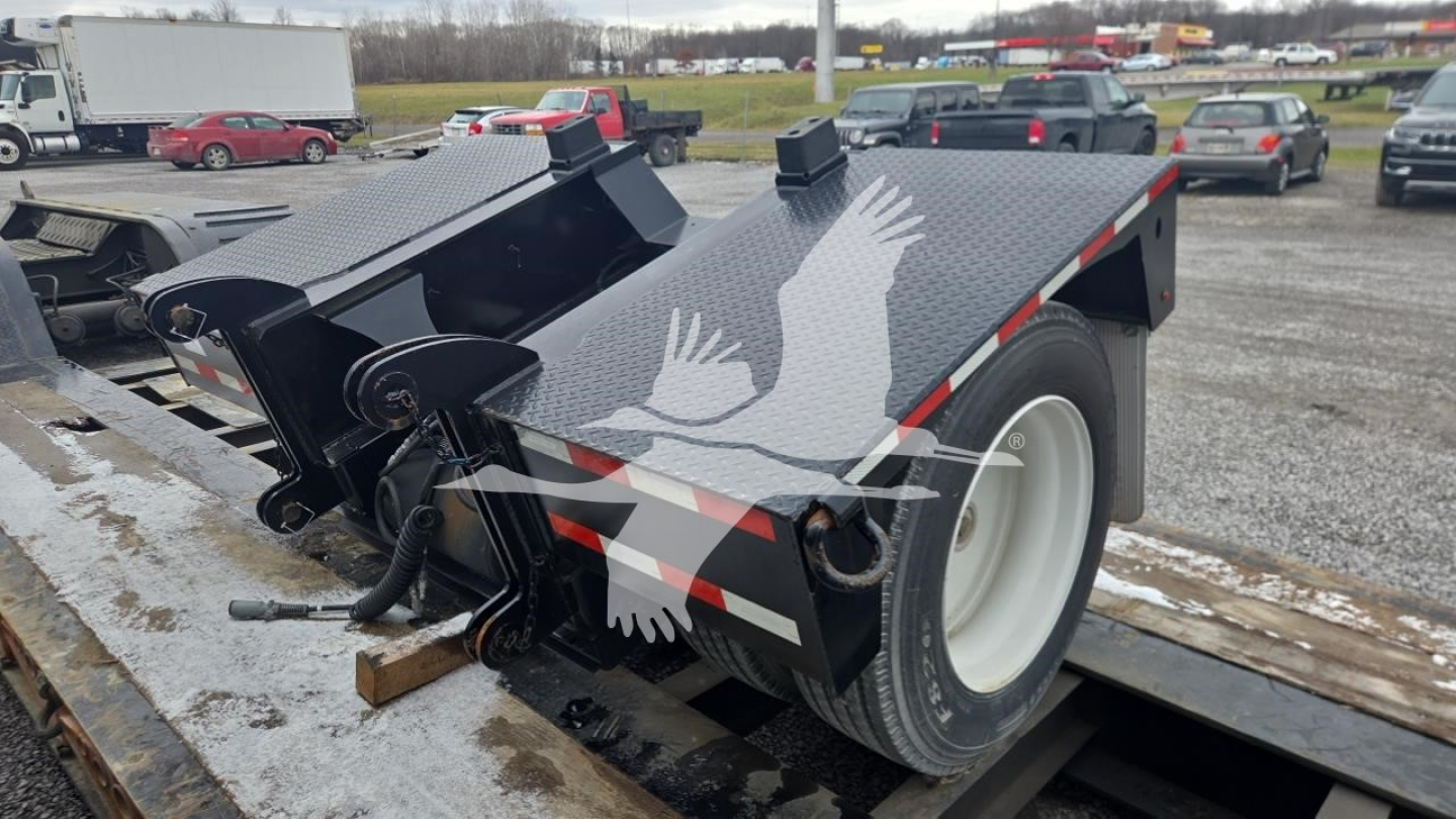 Trailer showing dual-axle lowboy with black metal frame and white wheel, top deck with textured surface, hydraulic ramps, and safety chains; some equipment visible near the hitch.