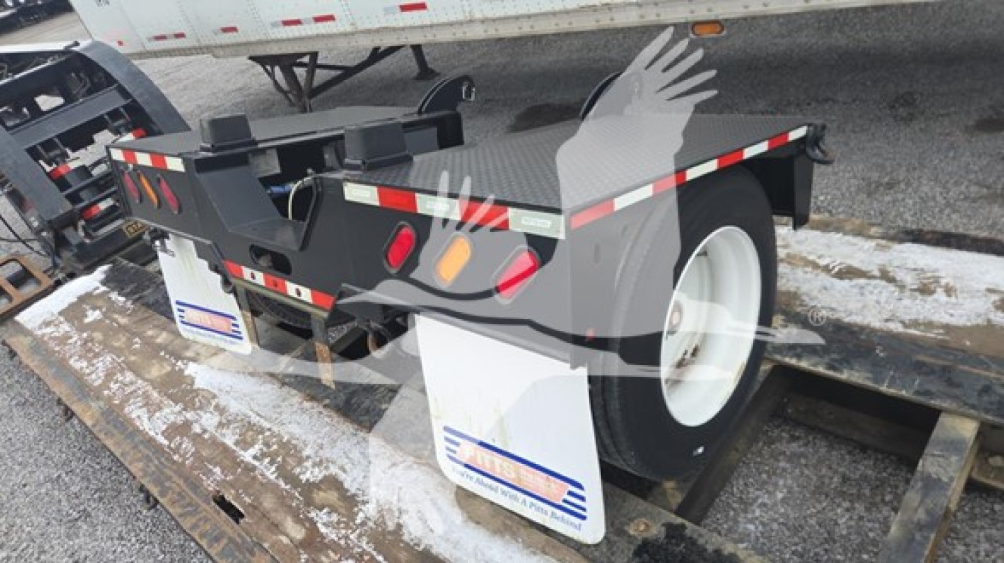 Lowboy trailer axle and rear section showing white wheel, black frame, and reflective red/white safety tape with a small license plate area.