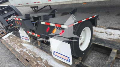 Trailer rear view showing left and right fenders, wheel, and reflective safety tape on a lowboy trailer. Visible text includes stock tag and brand stickers; license plate area obscured.