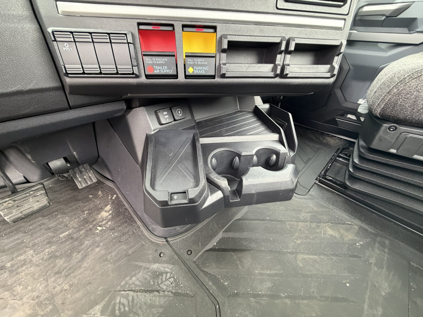 Cab interior of a 2027 Mack AN64T daycab showing dashboard switches, storage cubbies, and floor mat.