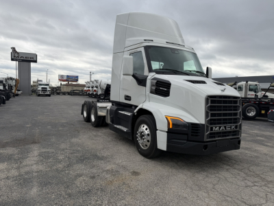 Truck cab of a white 2027 Mack AN64T in a dealership lot, front grille visible, with high sleeper roof and dual rear axles; Mack logo on grille.