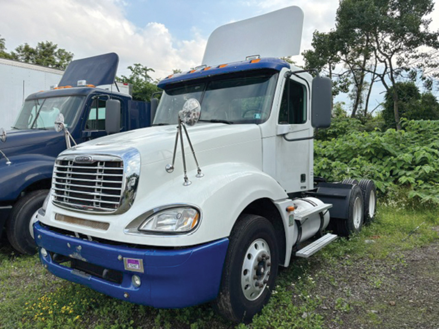 Truck engine bay with hood open on white Freightliner CL120 Columbia cab over chassis showing front grille and blue bumper.