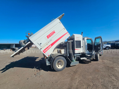 Truck chassis with dump hopper raised showing Elgin brand on side, Freightliner M2 106 in-service with open cab doors