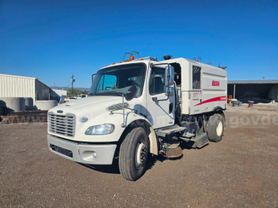 Freightliner M2 106 sweeperside view showing utility body and equipment storage, white cab, swept area undercarriage with brushes, no visible text on side asphalt lot