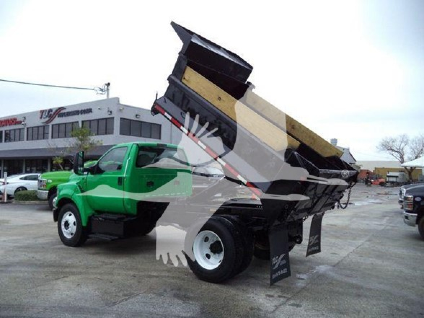 Ford F650 dump truck in-use with raised bed, green cab, white wheels, side view showing dumping bed and hydraulic mechanism.