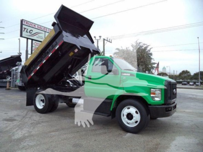 Green Ford F-650 dump truck with raised dumping bed in a dealership lot, side view showing cab and front wheel.