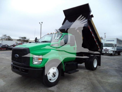 Green Ford F-650 dump truck with raised bed and black dump box, front view in a dealership lot.