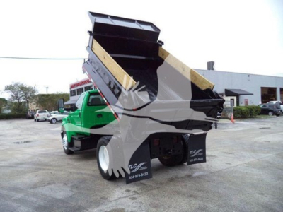 Dump truck bed in raised position on a 2017 Ford F650 SD used truck with green cab and front view, rear hydraulic lift with stakes.