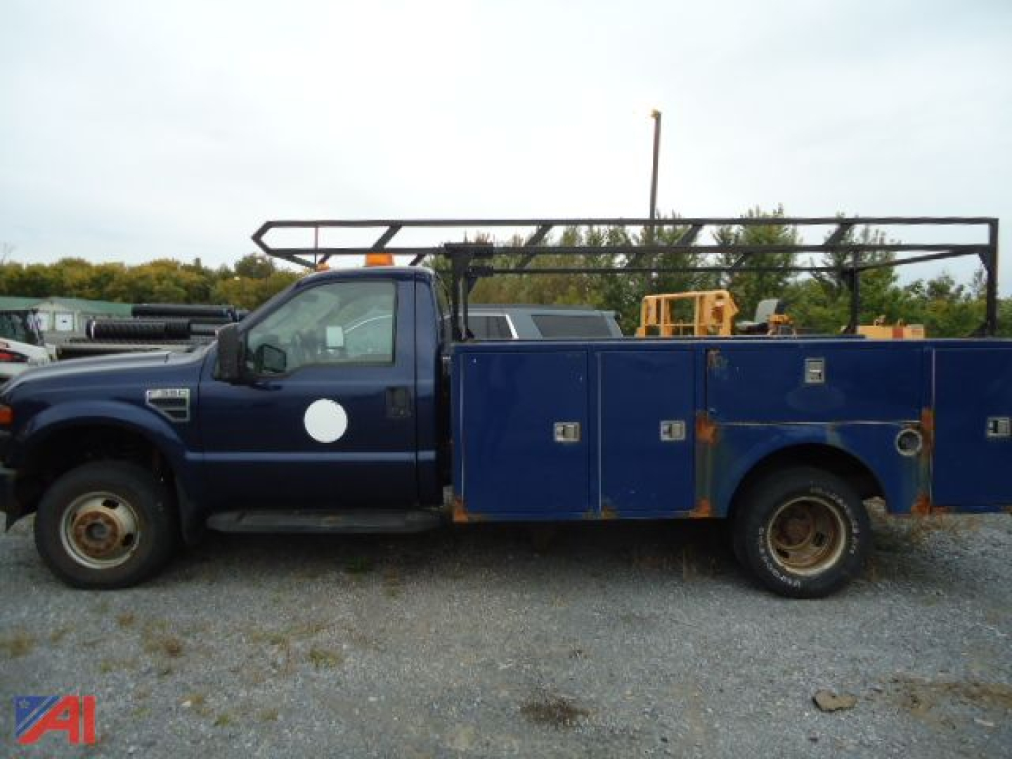 Ford F-350 Super Duty service truck with dual rear wheels, blue utility bed, side compartments, and rack on top in a gravel lot.