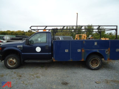 Ford F-350 Super Duty service truck with dual rear wheels, blue utility bed, side compartments, and rack on top in a gravel lot.