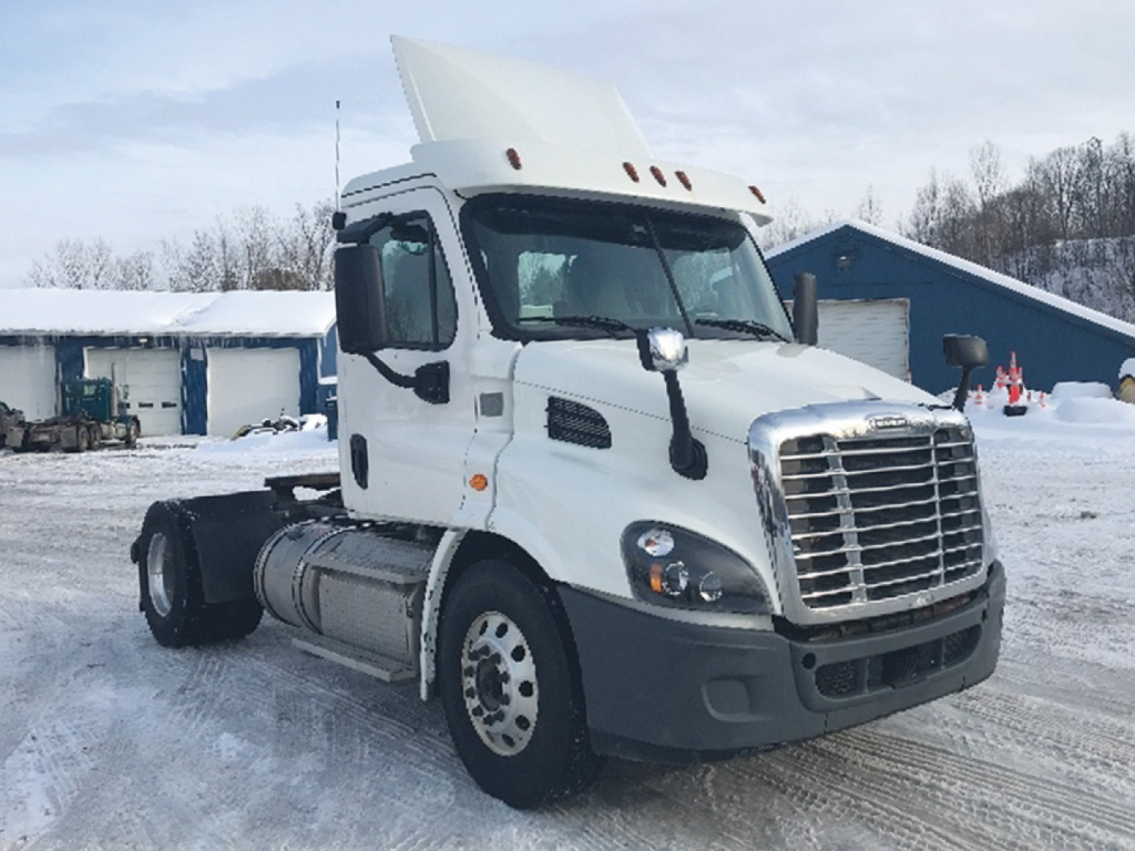 Freightliner Cascadia Daycab tractor cab in snow, front grille with large chrome bars, white exterior, no trailer attached, cab-only view.