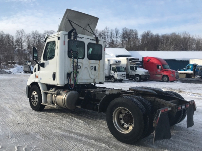 Truck chassis and cab of a Freightliner Cascadia113 tractor with raised hood and exposed cabling, in a snow-covered lot.