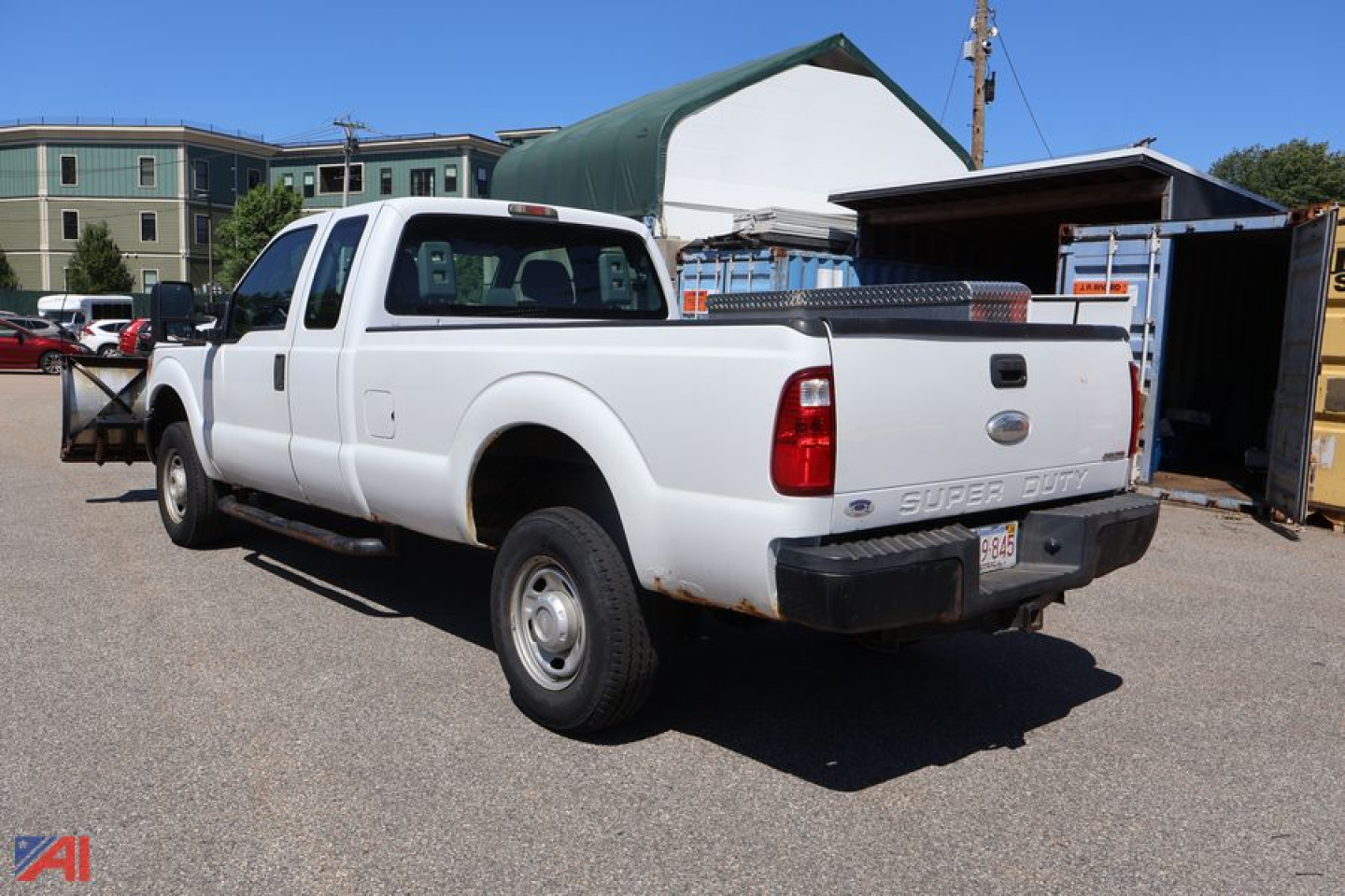 Ford F-250 Super Duty extended cab pickup with plow setup in a used truck lot, rear view showing tailgate and bed tool box.