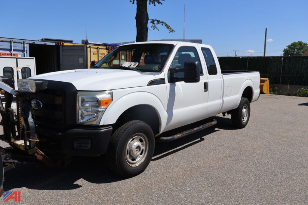 Ford F-250 Super Duty pickup with extended cab and plow in a lot showing front grille and side view.