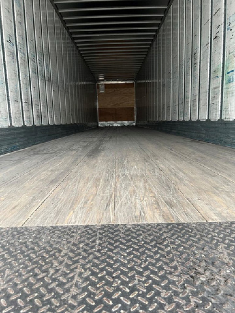 Interior of a 2014 utility van trailer showing empty box with wooden floor and metal sides; rear opening with diamond plate threshold.