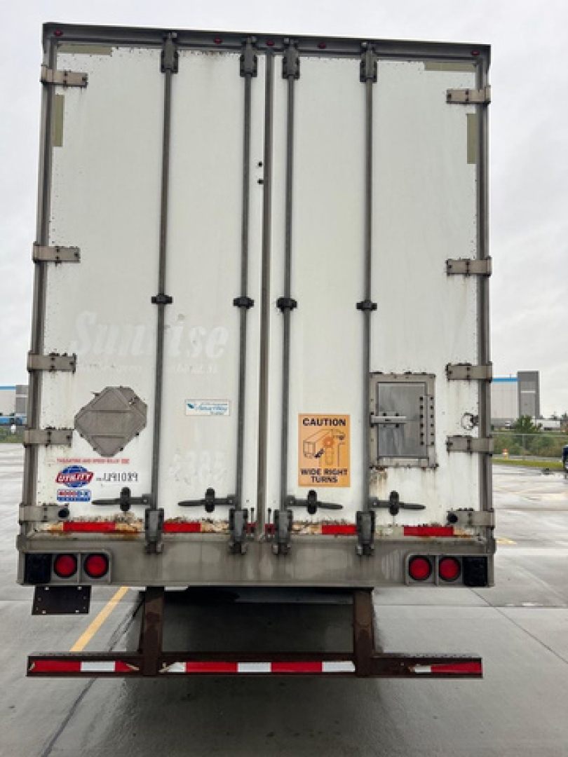 Rear view of a white utility van trailer with double doors, caution sticker, and various labels.