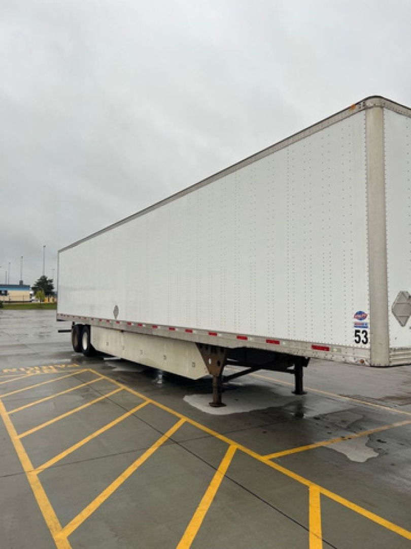 Utility van trailer side view showing white fiberglass box with landing gear and bumper in a parking lot.