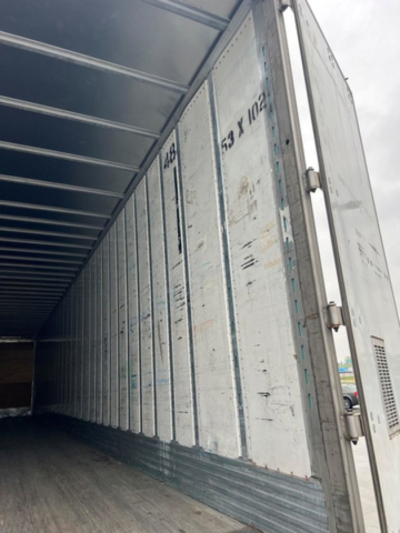 Interior of an open utility van trailer showing corrugated metal walls and ribbed ceiling with vertical door hinges.