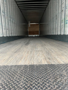 Interior of a 2014 utility van trailer showing empty box with wooden floor and metal sides; rear opening with diamond plate threshold.