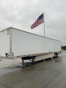 Utility van trailer in a parking lot with American flag flying on a pole.