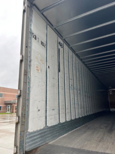 Trailer interior showing empty cargo space with corrugated metal side walls and ribbed ceiling, numbers 53, 1023, and 48 printed on the panels.
