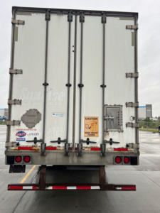 Rear view of a white utility van trailer with double doors, caution sticker, and various labels.