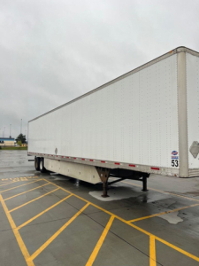 Utility van trailer side view showing white fiberglass box with landing gear and bumper in a parking lot.